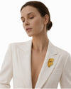 Woman wearing a sculptural PVD real gold plated statement face brooch on a white blazer by Eda Jewels Dubai
