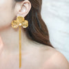Eda Jewels Dubai gold plated ginkgo leaf flower drop earrings with a pearl accent and long fringe chains worn by a model