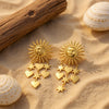Sora gold plated celestial sunburst statement earrings featuring dangling star and heart charms resting on the sand