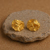 maha gold plated textured crumpled round disc stud earrings resting on a raw stone background by Eda Jewels Dubai