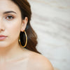 Zarina gold plated oversized classic hoop earrings with a high shine polished finish worn by a model by Eda Jewels Dubai.
